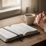 Open Bible, journal, and folded hands during quiet morning prayer