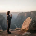 Person praying beside a stable rock above a wide valley
