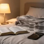 Open Bible, water, and lamp beside a bed prepared for restful prayer